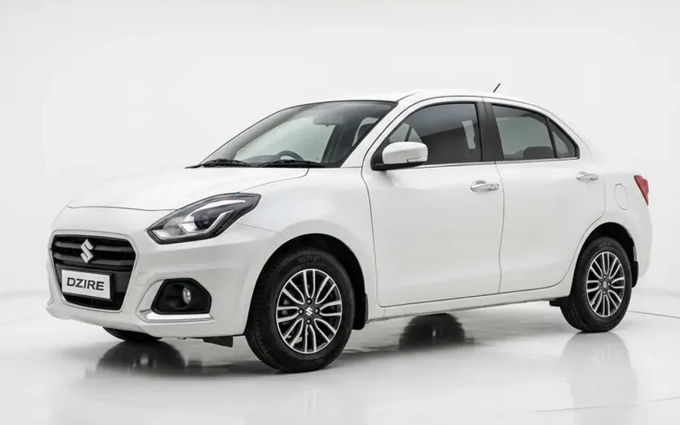 Three quarter front view of a clean white Swift Dzire class sedan, boot open showing two suitcases, plain paved backgrou