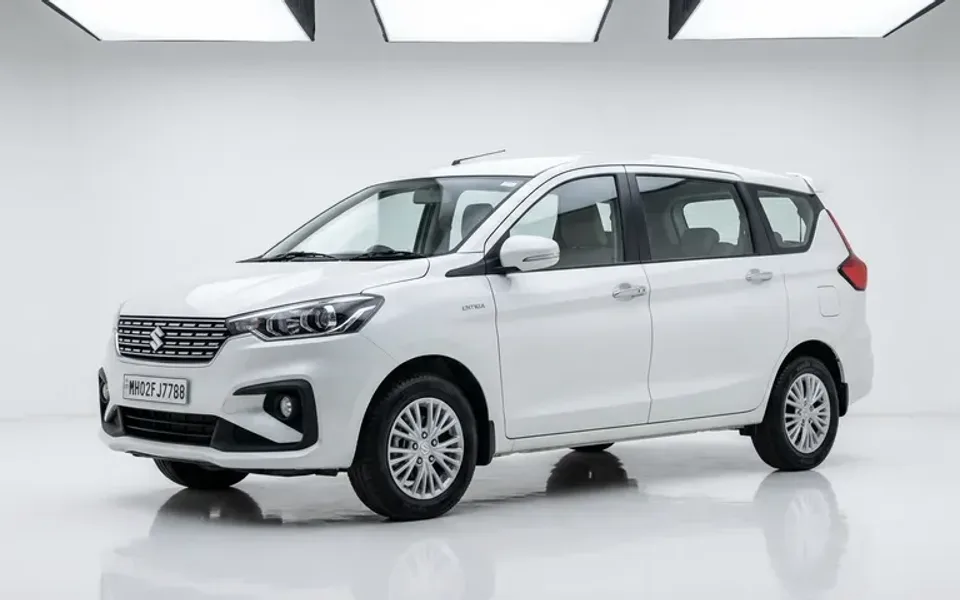 Three quarter front view of a clean silver Ertiga or Innova class SUV, rear door open, a family loading bags, plain pave